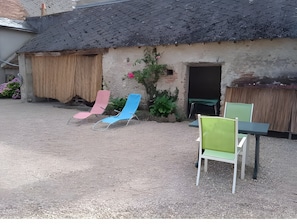Ein Gebäude mit einem Strohdach, einem Kieshof und Außenbestuhlung mit Stühlen und einem Tisch.