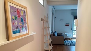 Un couloir avec un plancher en bois, une œuvre d’art encadrée au mur, une échelle blanche et un canapé à l’arrière-plan.