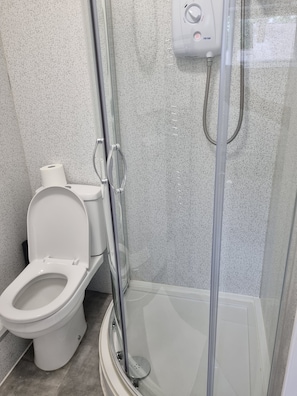 Ein Badezimmer mit Toilette, einer Duschkabine aus Glas und einem Händetrockner.
