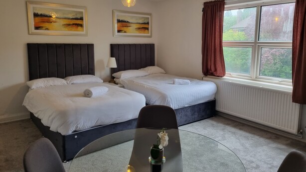 Ein Hotelzimmer mit zwei Betten, einem Schreibtisch mit Stuhl, einer Lampe und einem Fenster mit Vorhängen.