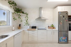 Eine moderne Küche mit weißen Schränken, einem Edelstahlkühlschrank und einem Fenster mit Blick auf eine Wüstenlandschaft.