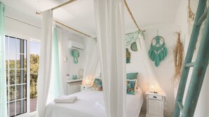 Un dormitorio con cama con dosel, una mesita de noche pequeña, aire acondicionado instalado en la pared y vistas a través de un ventanal.
