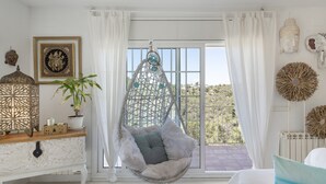 Una habitación con una silla colgante, una planta en maceta, decoración en la pared y vistas amplias a través de grandes ventanales.