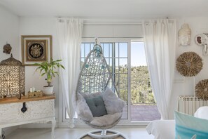 Una habitación con una silla colgante, una planta en maceta, decoración en la pared y vistas amplias a través de grandes ventanales.