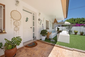 Eine Terrasse mit einer weißen Couch, Blumentöpfen und einem kleinen Gartenbereich.