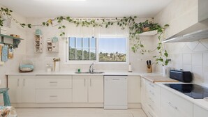 Una cocina moderna con armarios blancos, lavavajillas, ventana con vistas y plantas decorativas.