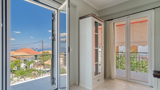 A room with a sliding glass door, a wardrobe, and a balcony with a view of buildings and trees.