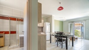 A modern kitchen with a dining area, a glass shower enclosure, and a balcony with a view.