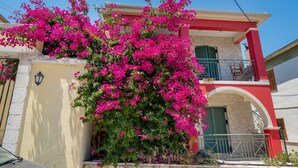 A building with a balcony, a stone wall, and a pink flowering bush.