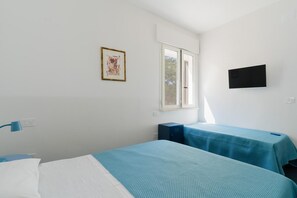 Una stanza con due letti, una finestra, una TV a schermo piatto e un quadro appeso al muro.