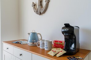 Un piano di lavoro in cucina con una macchina da caffè, due tazze, un bollitore, una scatola di tè Twinings e una confezione di caffè.