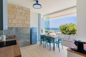 Una cucina moderna con un frigorifero blu, un'area pranzo con sedie color acquamarina e un'ampia finestra vista mare.