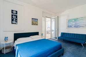 Una camera da letto con un letto, un divano blu, un tavolino e opere d'arte alle pareti.