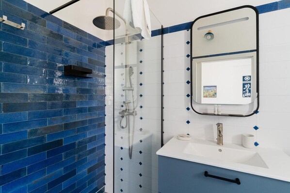 A bathroom with a glass shower enclosure, a white sink, and a mirror.