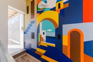 Un corridoio con un murale astratto colorato, una scala e una porta che dà su uno spazio all'aperto.