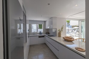 Eine moderne Küche mit weißen Schränken, einem Geschirrspüler und einem großen Fenster mit Blick auf eine Sitzgelegenheit im Freien.