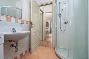 Un baño con lavabo, espejo, ducha y suelo de baldosas.