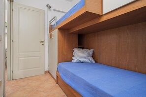 Ein Einzelbett mit blauer Matratze und gestreiftem Kopfkissen in einem Zimmer mit Holzbettgestellen darüber.