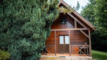 Eine Holzhütte mit Satteldach, einer Haustür und einer kleinen Veranda mit Geländer.