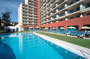 Un hotel con piscina, diversi balconi e lettini prendisole.