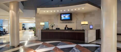 Zona de recepción de un hotel con diseño moderno, que incluye un mostrador de recepción, una pantalla de televisión y un suelo con estampado.