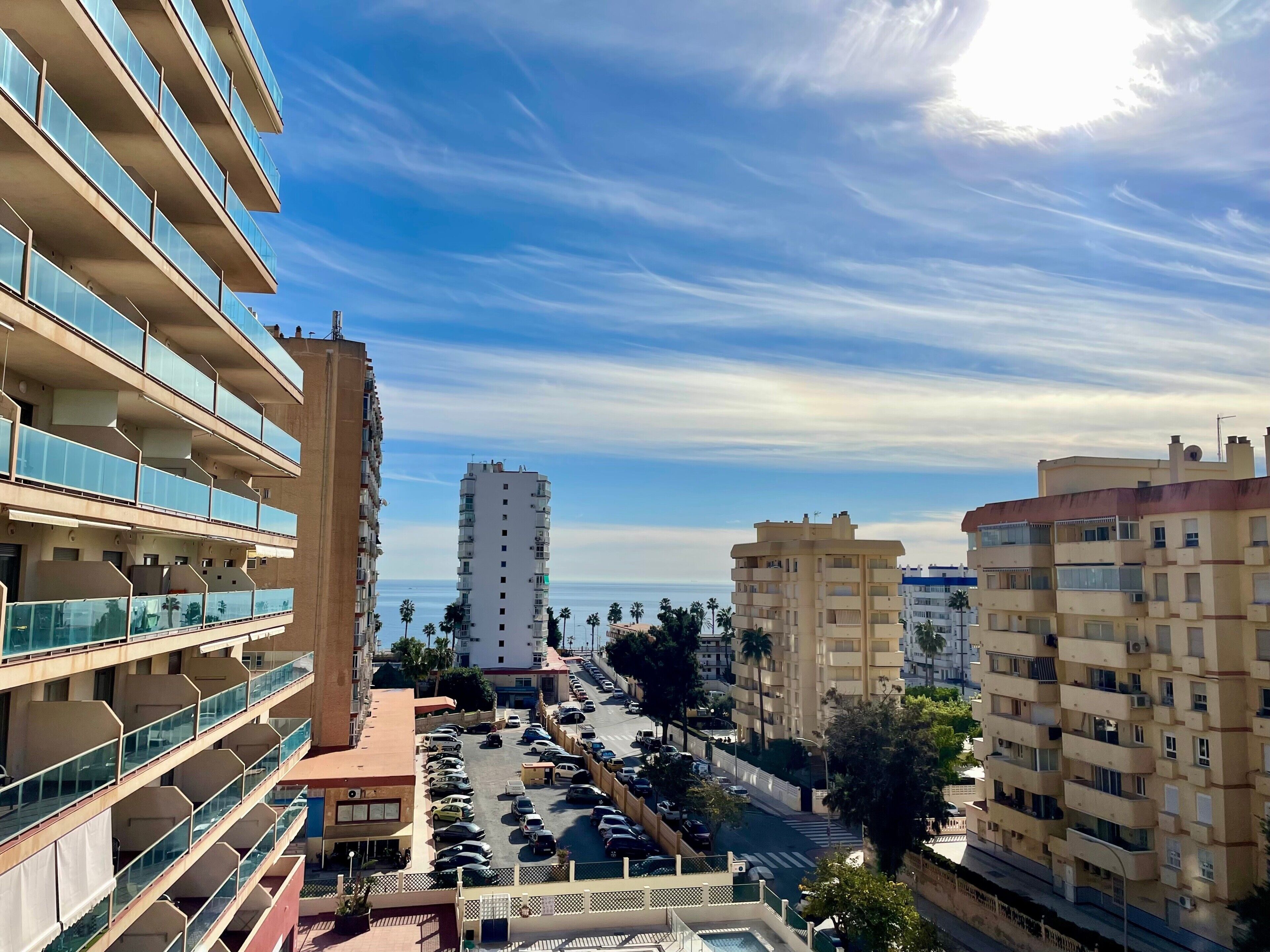 Un edificio residenziale a più piani con balconi, un parcheggio e vista libera sul mare.