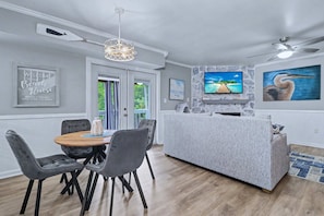 Ein modernes Wohnzimmer mit Kamin aus Stein, einem an der Wand befestigten Fernseher und einem Essbereich mit Holztisch und Stühlen.