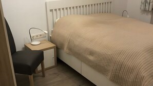 Quarto com cama, mesa de cabeceira com abajur, uma cadeira e guarda-roupa.