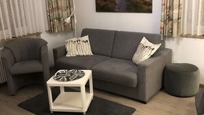 Uma sala de estar moderna com um sofá cinzento, duas almofadas estampadas, uma mesinha de apoio branca e um banquinho redondo.