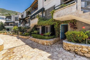 Un edificio moderno con fachada de piedra, balcones con plantas y un patio empedrado.