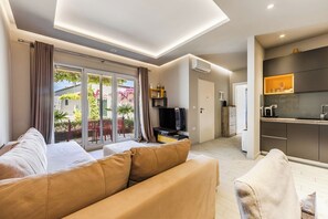Ein modernes Wohnzimmer mit einer Couch, einem Fernseher und einer Küchenzeile mit Arbeitsplatte und Schränken.