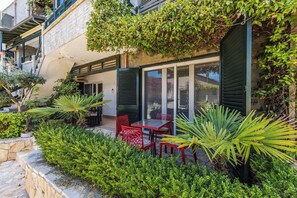 Un edificio con fachada de piedra, un balcón con plantas y un patio con mesa y sillas.