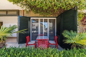 Un patio con una mesa y sillas, rodeado de vegetación y vistas a través de un ventanal.