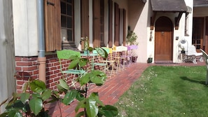 Ein Backsteinhaus mit Veranda, Außenbestuhlung und einem Rasenstück.