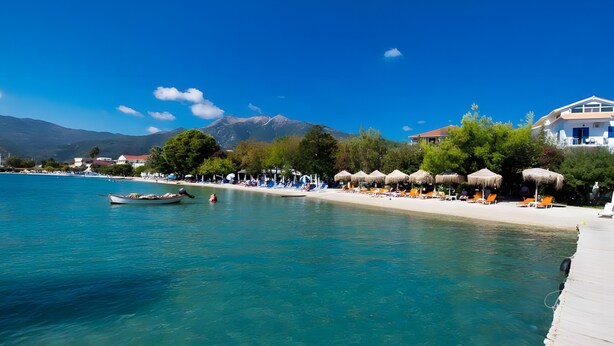 A coastal beach scene with clear turquoise water, a row of sun loungers, and a wooden pier extending into the sea. - Mati Sea View Apartment with Sea View, Wi-Fi, and Air Conditioning (Nydri)