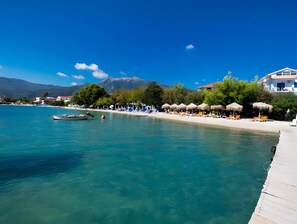 A coastal beach scene with clear turquoise water, a row of sun loungers, and a wooden pier extending into the sea. - Mati Sea View Apartment with Sea View, Wi-Fi, and Air Conditioning (Nydri)