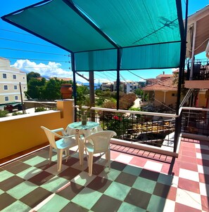 A balcony with a checkered floor, a table with chairs, and a large umbrella. - Mati Sea View Apartment with Sea View, Wi-Fi, and Air Conditioning (Nydri)