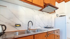 A kitchen with a marble backsplash, stainless steel sink, wooden cabinets, and a white refrigerator. - Mati Sea View Apartment with Sea View, Wi-Fi, and Air Conditioning (Nydri)