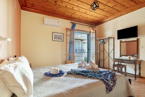 Un dormitorio con techo de madera, cama con ropa de cama blanca, televisor y ventana con vista a las montañas.