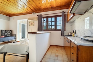 Una cocina compacta con armarios de madera, encimera de mármol y ventana con cortinas.