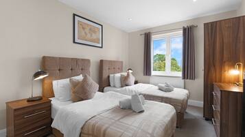 Quarto de hotel com duas camas, uma mesinha de cabeceira de madeira, cômoda e janela com cortinas.