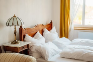 Una cama bien tendida con sábanas blancas, cabecera de madera y mesita de noche con lámpara.