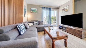A modern living room with a grey sofa, wooden panel wall, and a large TV.