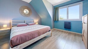 A bedroom with a bed, bedside lamps, a wall-mounted heater, and a window with curtains.