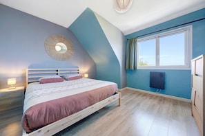 Ein Schlafzimmer mit Bett, Nachttischlampen, einem Wandheizkörper und einem Fenster mit Vorhängen.