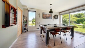 A modern kitchen with a dining table, chairs, and a view of greenery outside.