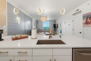 A modern kitchen with a central island, pendant lighting, and a view to a balcony. - Emerald Isle 1805 - JUST COMPLETELY RENOVATED! Beach chair service included! (Panama City Beach)