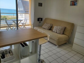 Quarto com sofá, mesa de jantar, vista para o mar e piso de azulejos.