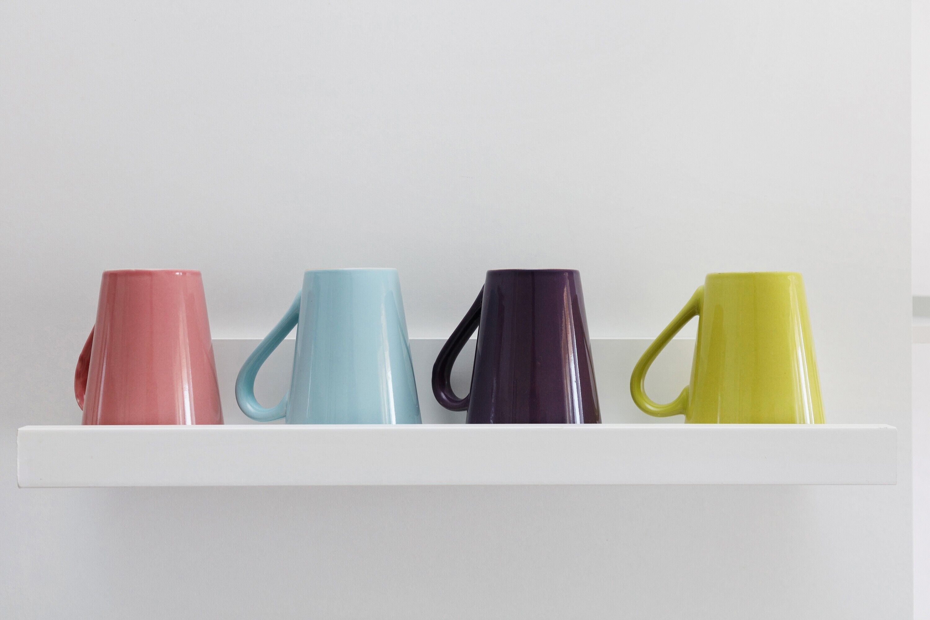 A white shelf with four ceramic mugs in different colors.