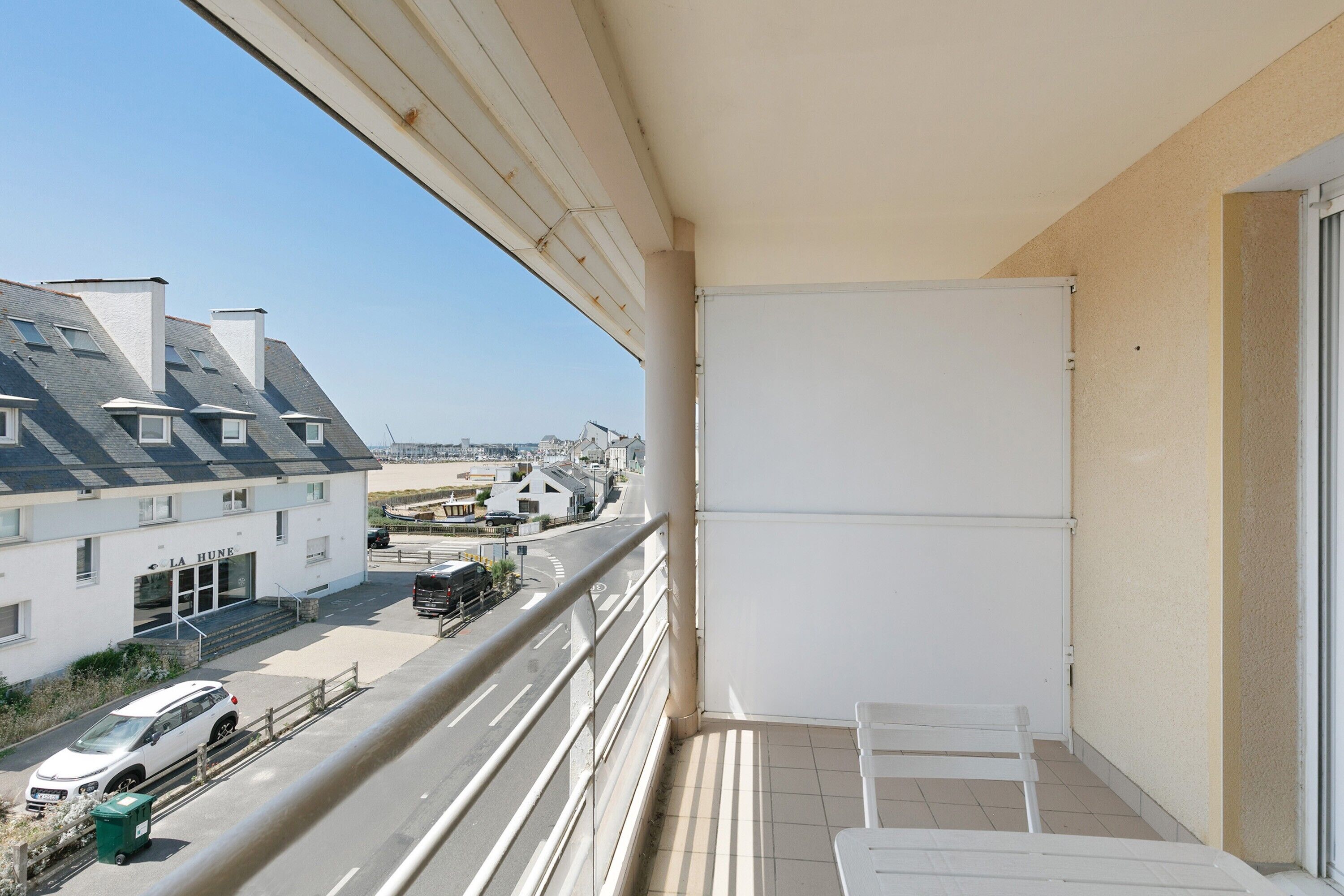 A balcony with a view of a street, a building with a sign 'LA HUNE,' and a parked car.